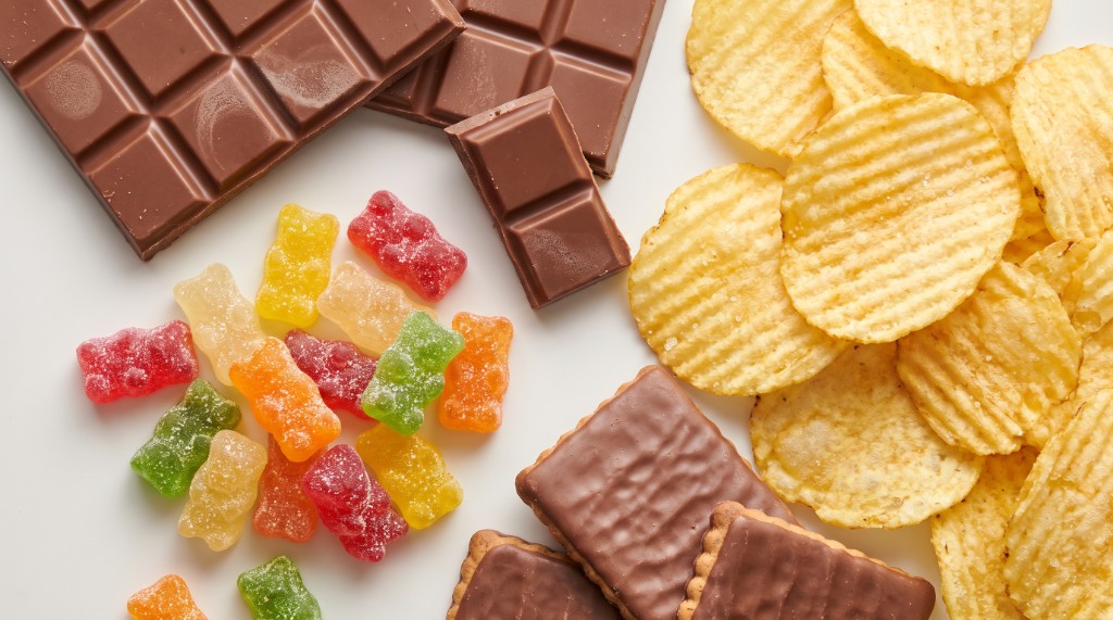 Schokolade, Gummibärchen, Kekse und Chips auf weißem Untergrund